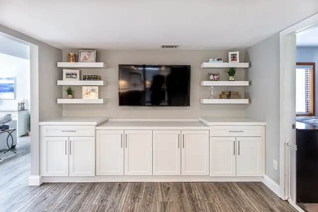 Built-in entertainment wall with white shaker base cabinets, a quartz top and floating shelves