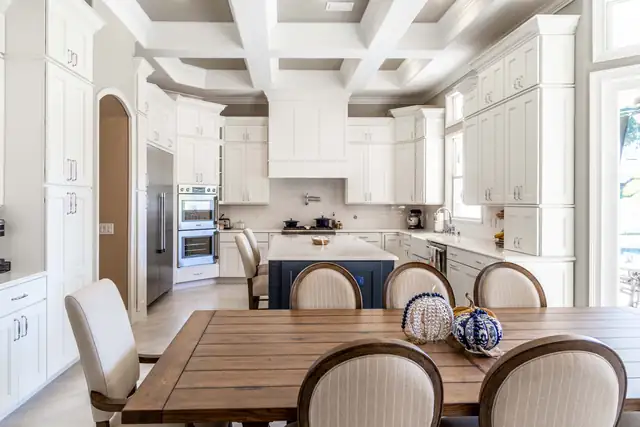 Kitchen and dining area with a coffered ceiling, white cabinetry, double wall ovens and a navy island