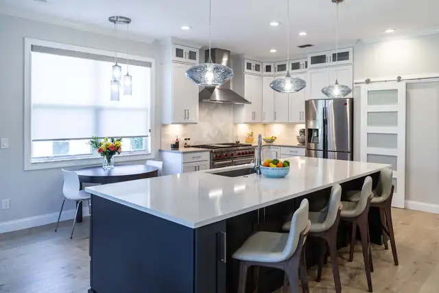 Remodeled kitchen with white cabinets, a navy island with white quartz top, blue glass pendants and a chevron tile backsplash