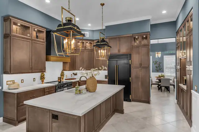 Kitchen with stained wood cabinets to the ceiling, black and brass lantern pendants and a white quartz island
