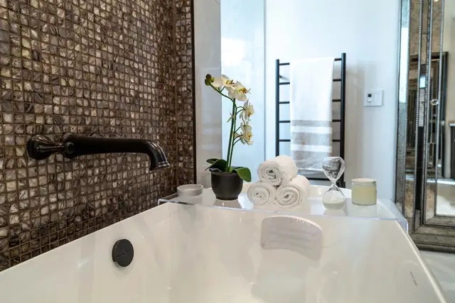 Master bath detail with a soaking tub, bronze glass mosaic accent wall and matte black wall-mounted faucet