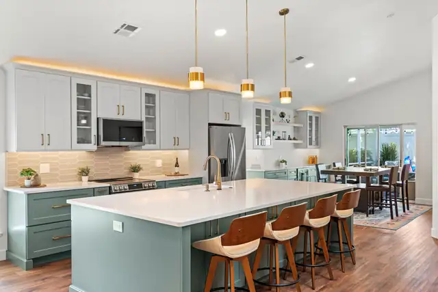Kitchen with a sage green island, white quartz top, brass pendants, light gray shaker cabinets and wood counter stools