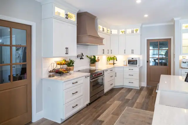 White kitchen with glass-front upper cabinets, a taupe range hood, under-cabinet lighting and wood-look plank floors