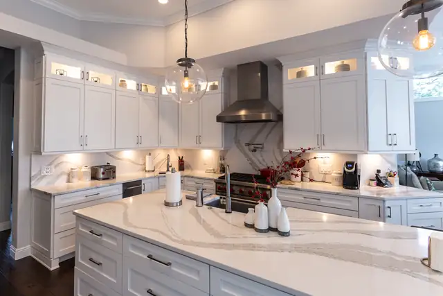 White kitchen by Stevens Kitchens with a stainless hood, a marble-look quartz backsplash and island, and a glass globe pendant