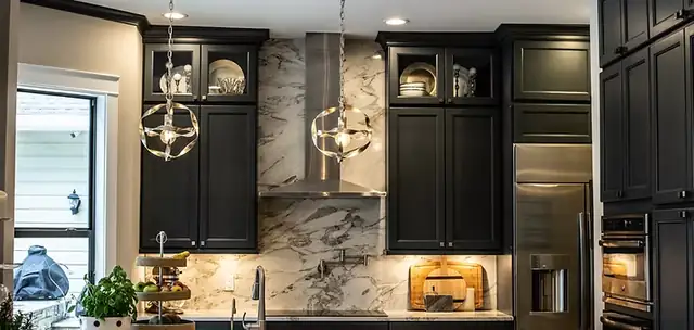 Kitchen with black shaker cabinets to the ceiling, glass-front uppers, a marble slab backsplash and stainless range hood