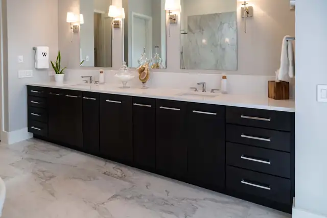 Master bath with a long black vanity, white quartz top, framed mirrors and marble-look floor tile