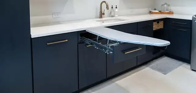 Laundry room with navy cabinets, a pull-out ironing board drawer, white quartz counter and undermount sink